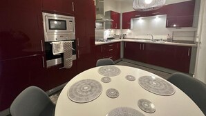 Una cocina moderna con armarios rojo oscuro, un horno de acero inoxidable, un microondas, una lámpara colgante y una mesa de comedor redonda con individuales.