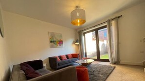 Un salón moderno con sofá, sillón y mesa de centro, un cuadro en la pared y un amplio ventanal corredero que da a un espacio exterior.