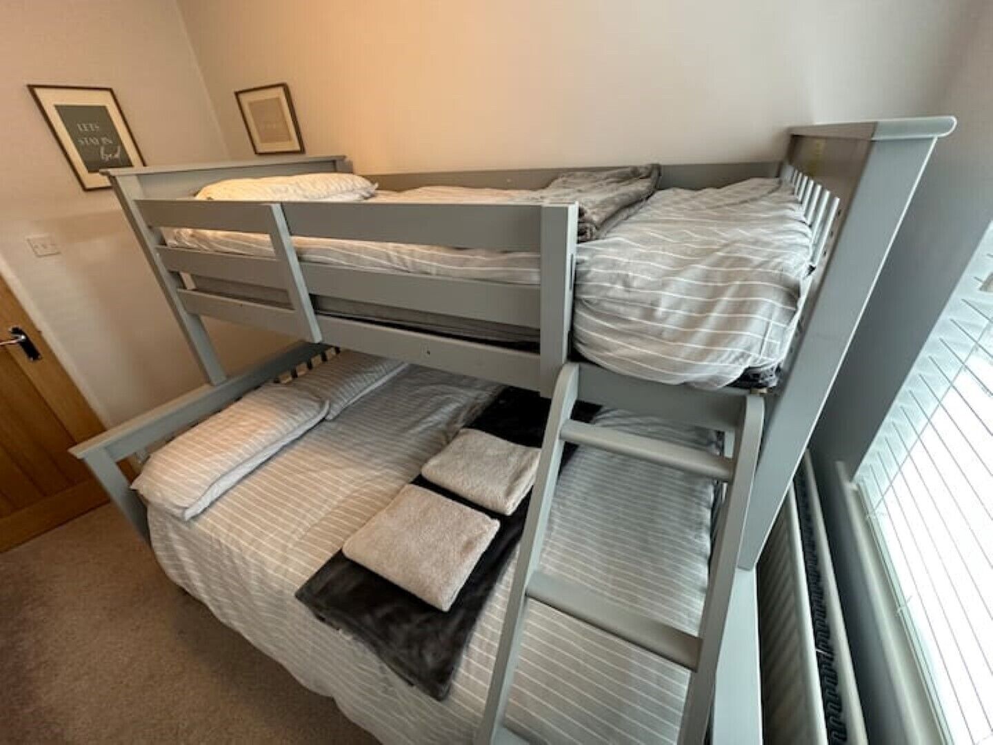 Une chambre avec un lit superposé, deux lits, une porte et une fenêtre avec des stores.
