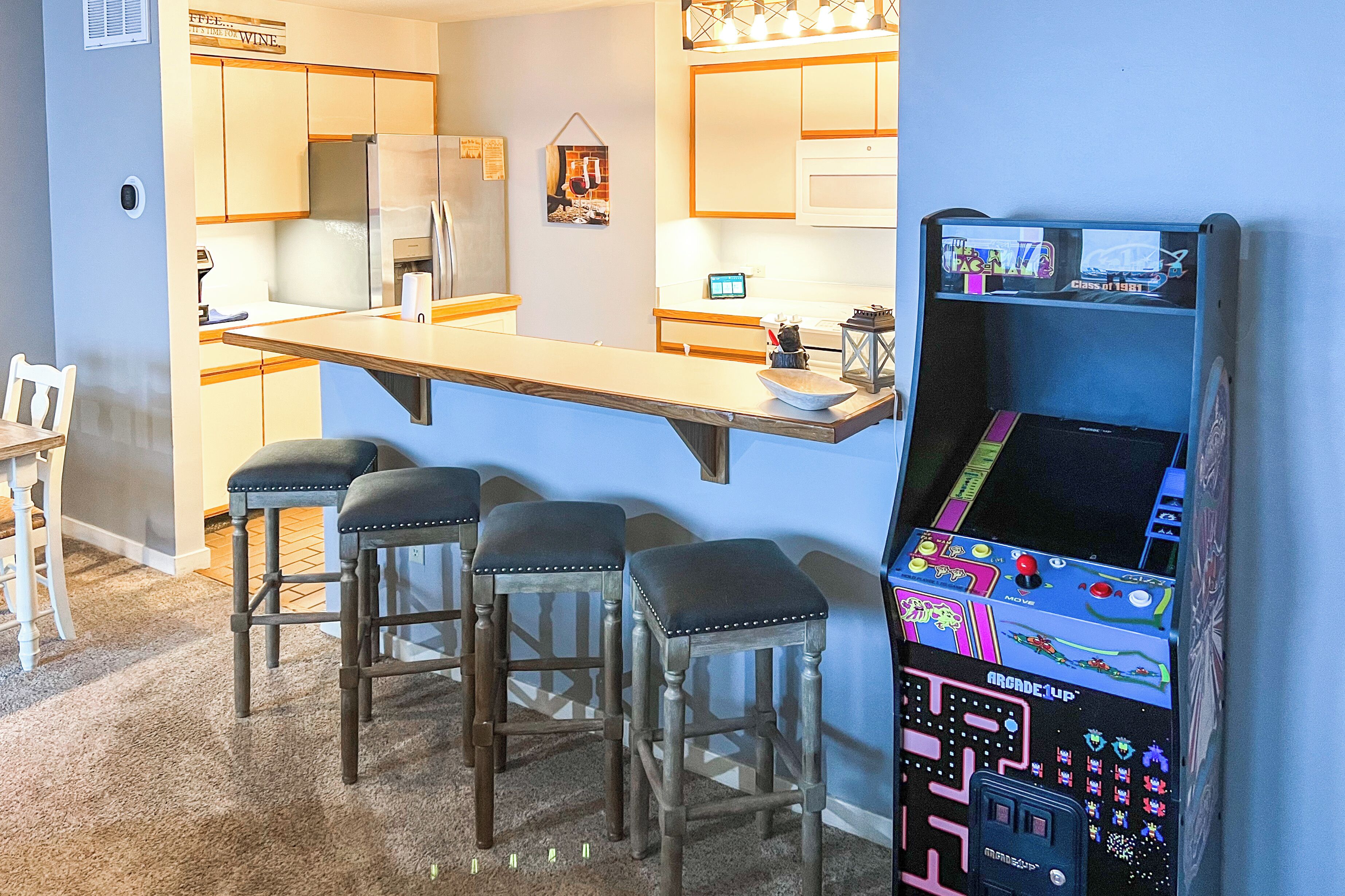 A kitchen with a bar area, stools, and a retro arcade machine.