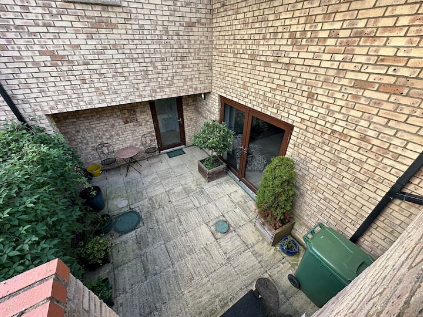 A courtyard with a brick wall, a glass door, and a small seating area with a table and chairs.