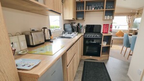 A compact kitchen with wooden cabinets, a built-in oven, a coffee machine, and a dining area with a table and chairs.