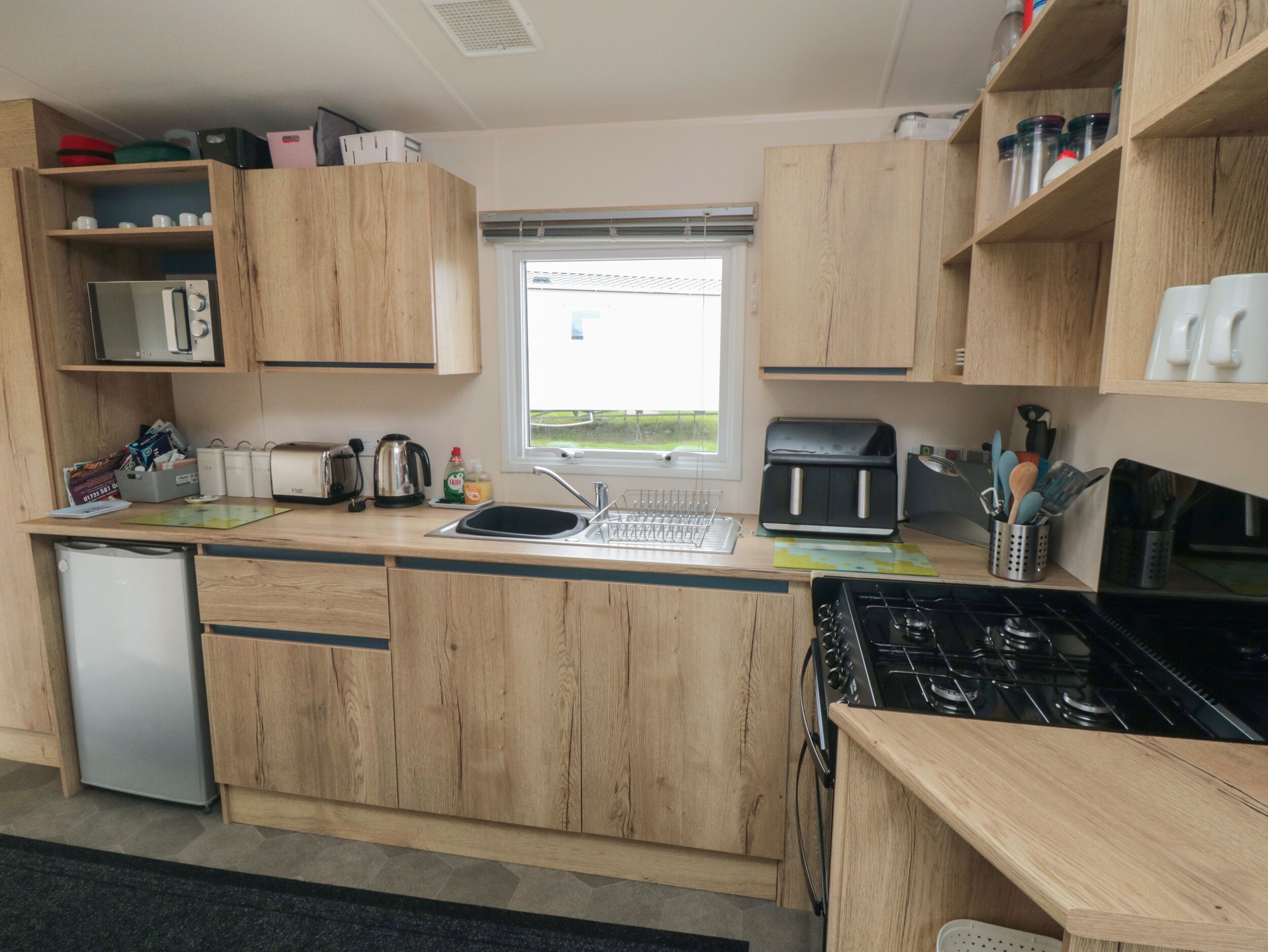 A compact kitchen with wooden cabinets, a built-in microwave, a toaster, a kettle, and a stove.