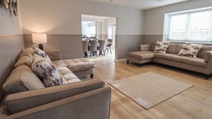 Una sala de estar moderna con un sofá modular, una chaise longue y un ventanal con persianas.