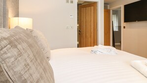 Un dormitorio con una cama, una puerta de madera, un televisor montado en la pared y una lámpara.