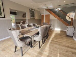 A dining area with a wooden table and upholstered chairs, a staircase, and a view of a garden. - The Birches (Windermere)