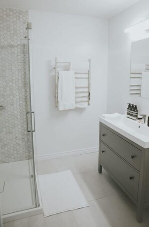 Une salle de bain moderne avec une douche à l’italienne en verre, un lavabo blanc agrémenté d’articles de toilette et un meuble-lavabo gris.