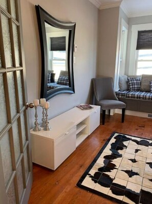 Um quarto com uma mesa consola branca, um espelho grande, uma cadeira, um sofá com almofadas xadrez e um tapete de couro de vaca.