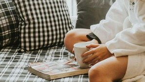 A person sitting on a plaid sofa with a book and a mug, in a room with a window and a white wall. - Suite n °1 au Séjour Knowlton (Knowlton)