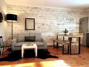 Un salon chaleureux avec un canapé à carreaux, une petite table blanche, une table à manger avec des chaises, un lampadaire noir et un tableau encadré accroché au mur.