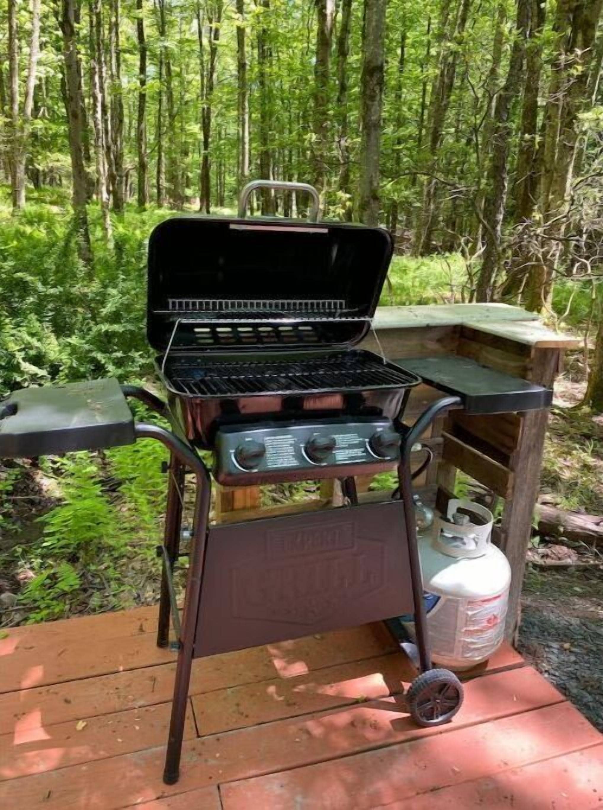 A portable grill with a control panel and a storage compartment, placed on a wooden deck surrounded by greenery.