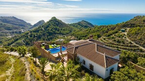 A villa with a swimming pool, surrounded by lush greenery and overlooking a coastal landscape.