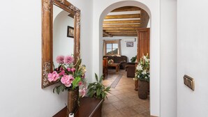 A hallway with a wooden-framed mirror, a vase with pink flowers, and a view into a living room with a sofa and a table.