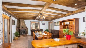 A spacious living area with a wooden ceiling, a fireplace, a dining table set for four, and a cozy seating area.