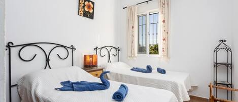 Una habitación de hotel con dos camas, una ventana con cortinas florales, un aire acondicionado instalado en la pared y un adorno decorativo en la pared.