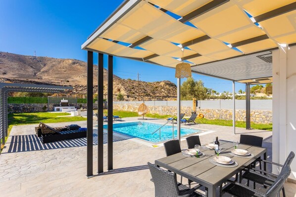Uma área de piscina moderna ao ar livre, com um terraço coberto, assentos e vista para a paisagem circundante.