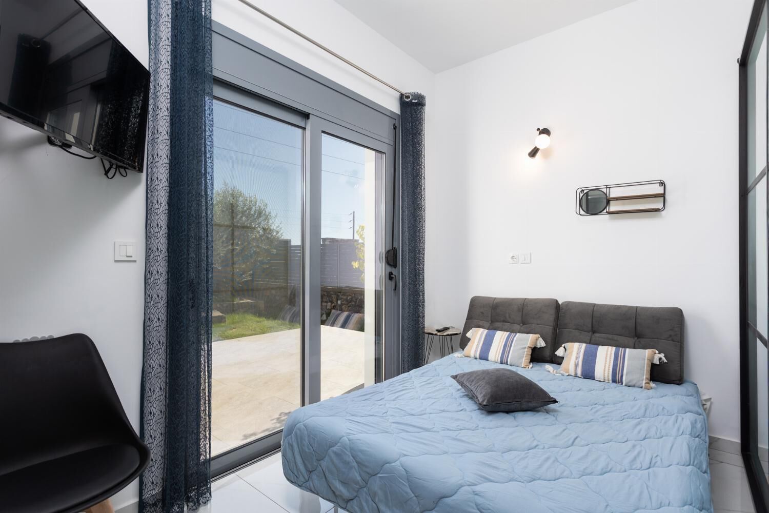 Ein Schlafzimmer mit Bett, Sessel, Fernseher und Fenster.
