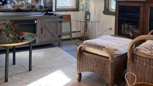 Een gezellige woonkamer met een televisie, rieten meubels en een boekenplank.