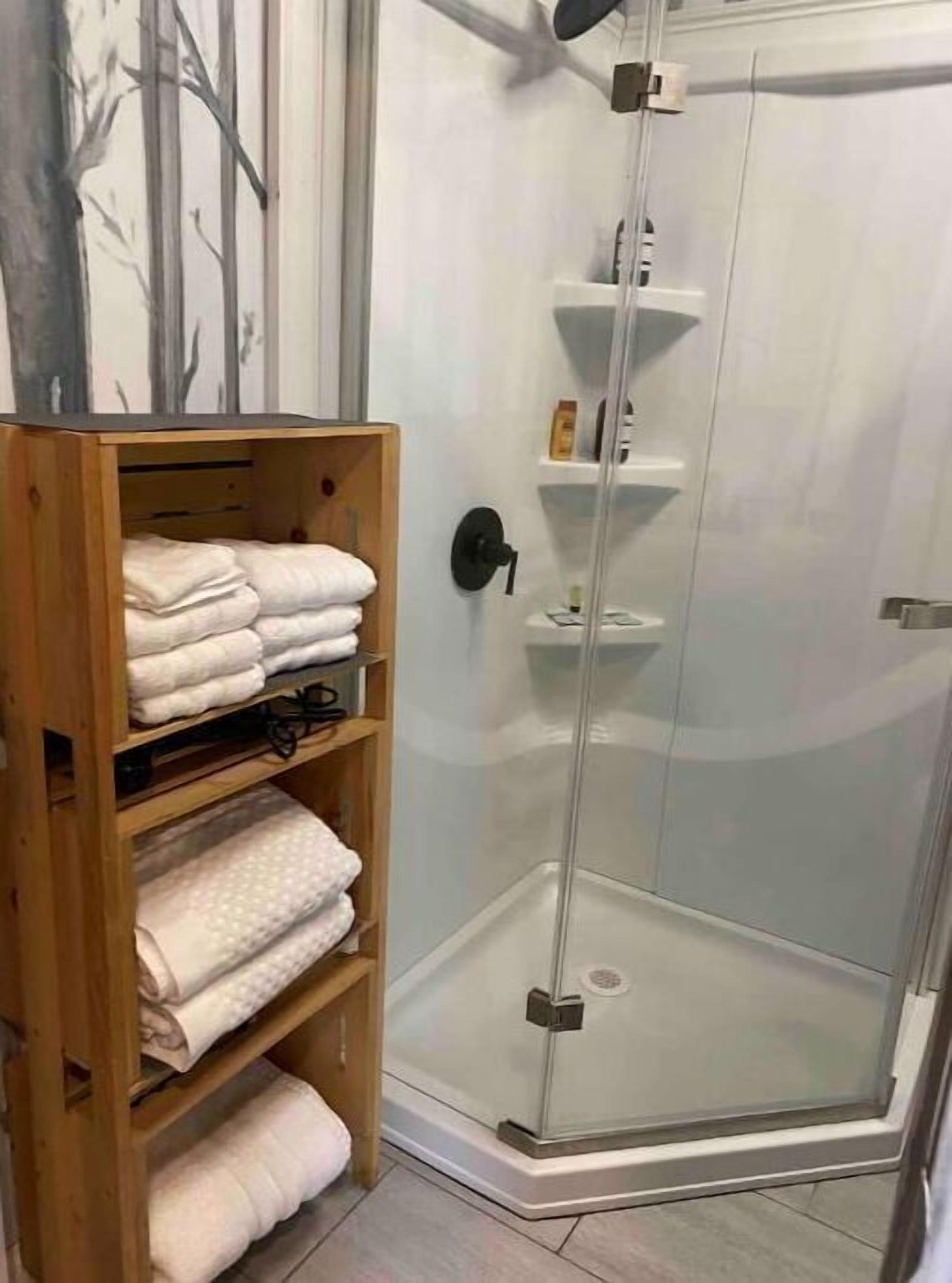 A shower area with a glass door, a wooden shelf with folded towels, and a tiled floor.