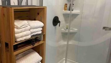 A shower area with a glass door, a wooden shelf with folded towels, and a tiled floor.