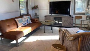 Een woonkamer met een bruine leren bank, een glazen salontafel, een rieten fauteuil en een televisie op een houten kast.