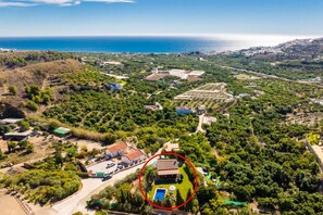An aerial view of a coastal property with a large building surrounded by lush greenery and a clear view of the sea.