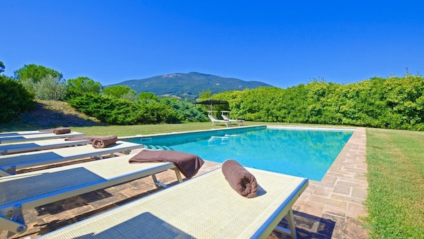 A swimming pool with lounge chairs and towels, surrounded by greenery and a mountain in the background. - Villa Piandisette - Four Bedroom Villa, Sleeps 10 (Cetona)