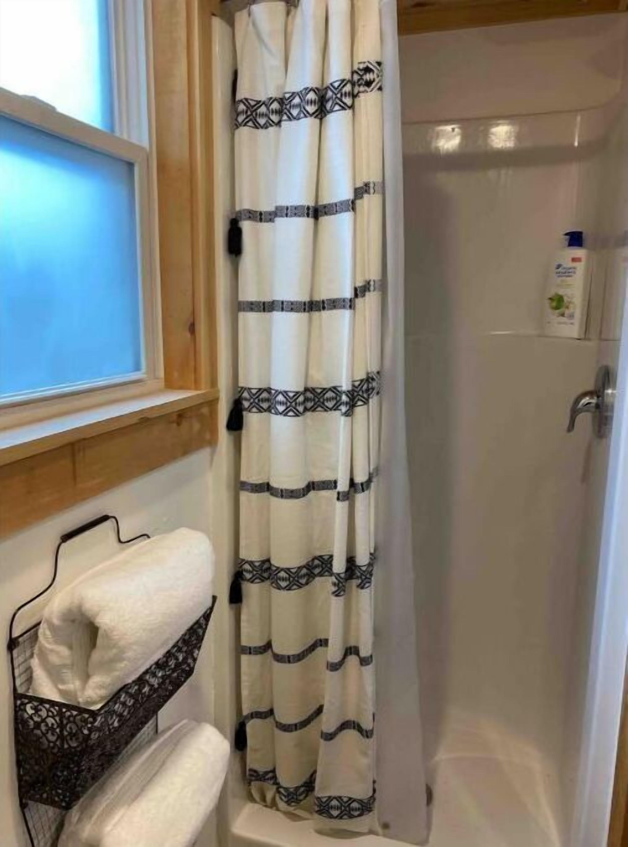 A bathroom with a shower curtain, a towel rack, and a bottle of shampoo on the wall.