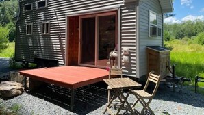 A small cabin with a sliding glass door, a patio with a table and chairs, and a wooden deck.