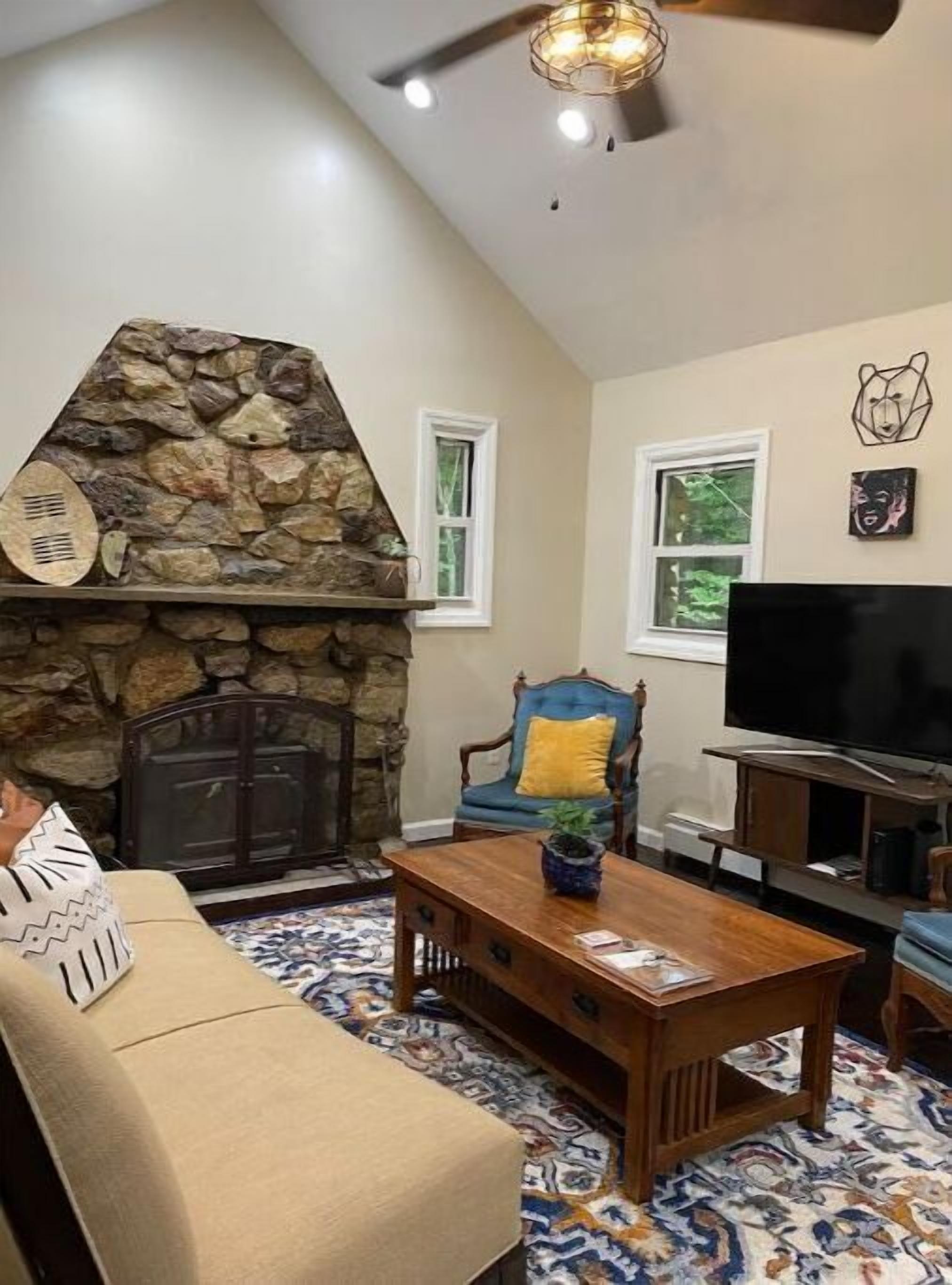 A living room with a stone fireplace, a television, a sofa, and a patterned rug.