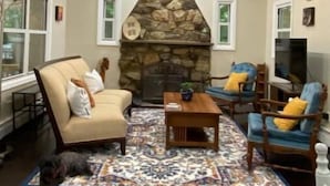 A living room with a stone fireplace, a ceiling fan, and a dog on a rug.