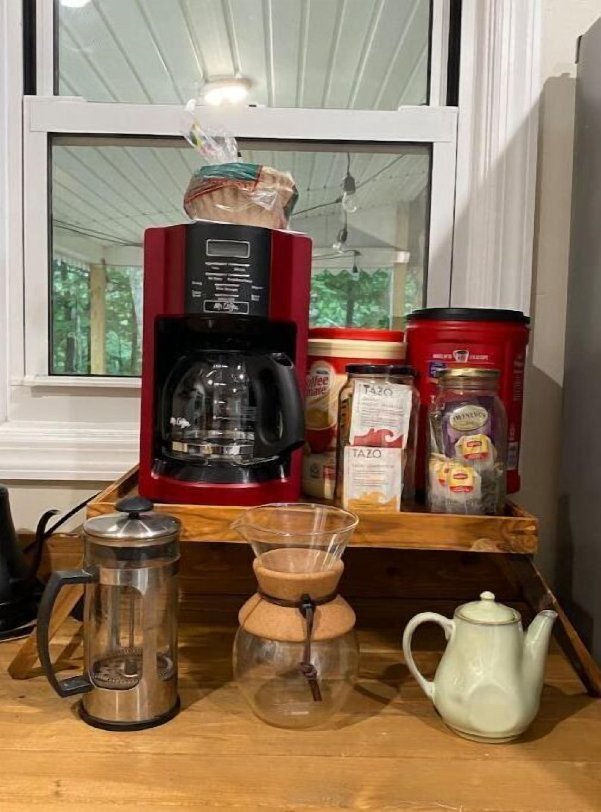 Un plan de travail de cuisine avec une machine à café, une verseuse en verre, une théière et divers produits alimentaires.