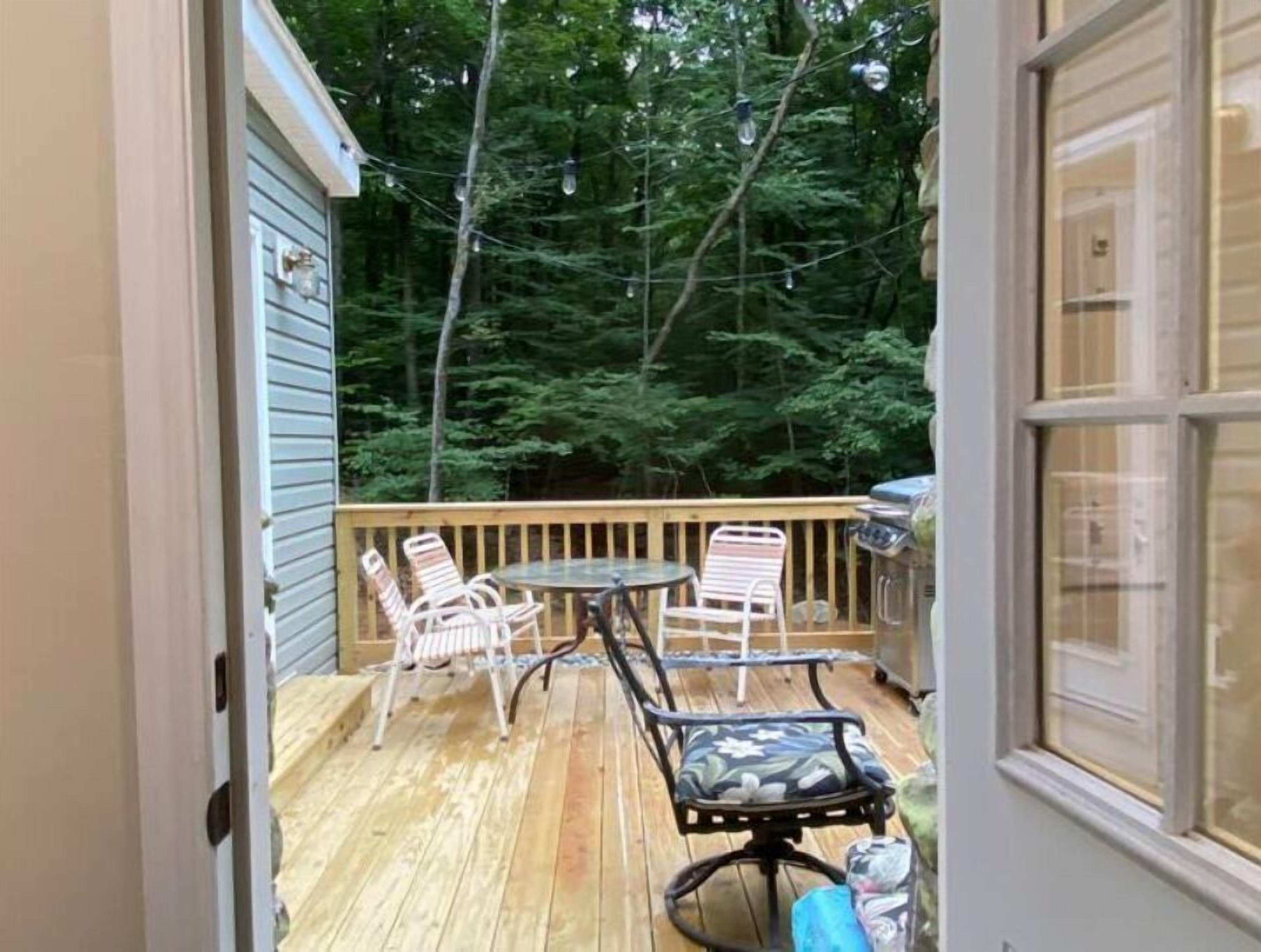 Un terrazzo in legno con mobili da esterno, un barbecue e vista su una zona boschiva.