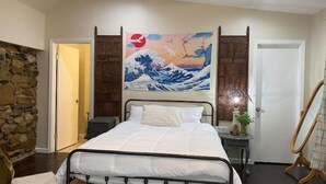 A bedroom with a bed, a wooden door, a stone wall, and a painting of waves.
