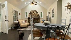 A dining area with a stone fireplace, a ceiling fan, and a dog walking through the space.