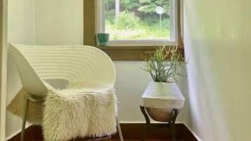 A narrow hallway with a window, a chair, and a small table with a plant.