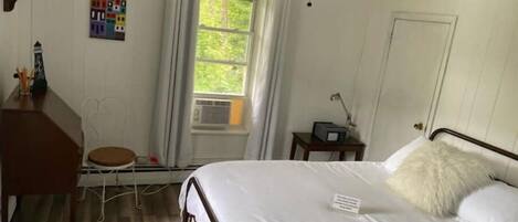 Et soveværelse med seng, skrivebord, stol, loftventilator, vindue og et billede på væggen.