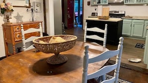 Een eetruimte met een houten tafel, witte stoelen, een rieten mand en een kroonluchter.