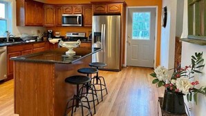 Una cocina con armarios de madera, un refrigerador de acero inoxidable, un microondas y una isla grande con taburetes.