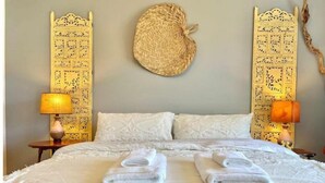 Una cama bien hecha con toallas dobladas, un tapiz de pared tejido y dos lámparas a cada lado.