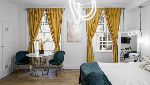 Ett modernt hotellrum med en säng, ett runt matbord med stolar och ett fönster med gardiner.