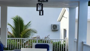 A covered outdoor seating area with a white table and chairs, a white railing, and a palm tree in the background. - Apartment for 4 with large pool



 (Samaná)