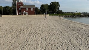 A sandy beach with footprints, a red building with a tower, and a water tower in the background. - Lakeside Oasis - Lake Erie Lakefront with Golf Cart (Luna Pier)