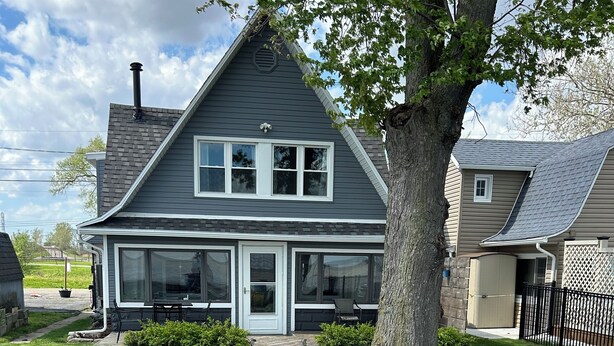 A two-story house with a covered patio area featuring outdoor furniture and a large planter with flowers. - Lakeside Oasis - Lake Erie Lakefront with Golf Cart (Luna Pier)