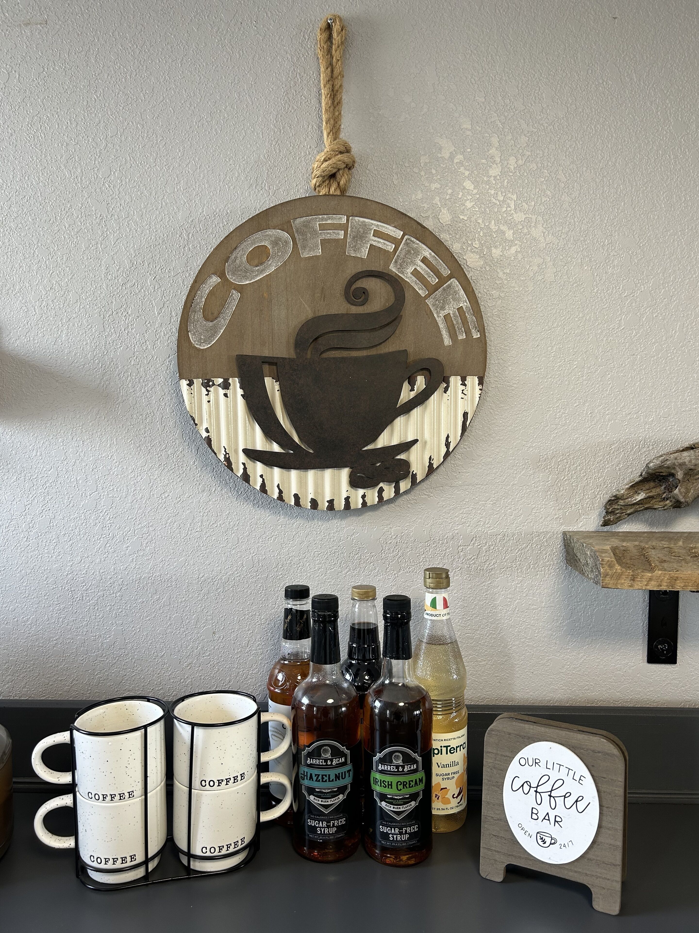 Une décoration sur le thème du café, avec un panneau en bois sur lequel est écrit « CAFÉ », des bouteilles de sirop sans sucre et des tasses disposées sur un comptoir.