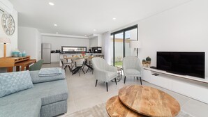 A modern living room with a sofa, chairs, a wooden coffee table, a TV, and a kitchen in the background. - Villa Paraíso - Holiday Villa with Private Pool By SCH (São Martinho do Porto)