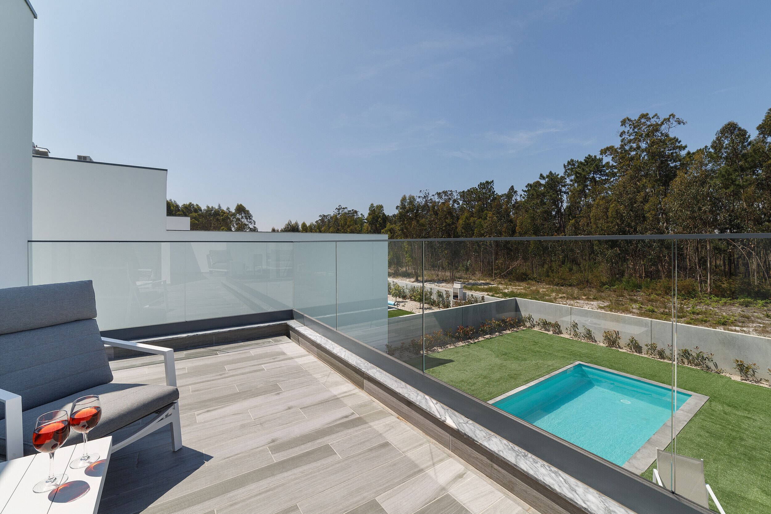 Una terraza moderna al aire libre con barandilla de vidrio, una piscina y un área de estar con mesa y sillas.