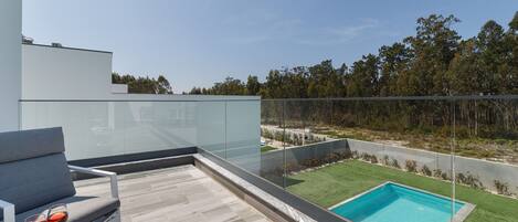 Una terraza moderna al aire libre con barandilla de vidrio, una piscina y un área de estar con mesa y sillas.