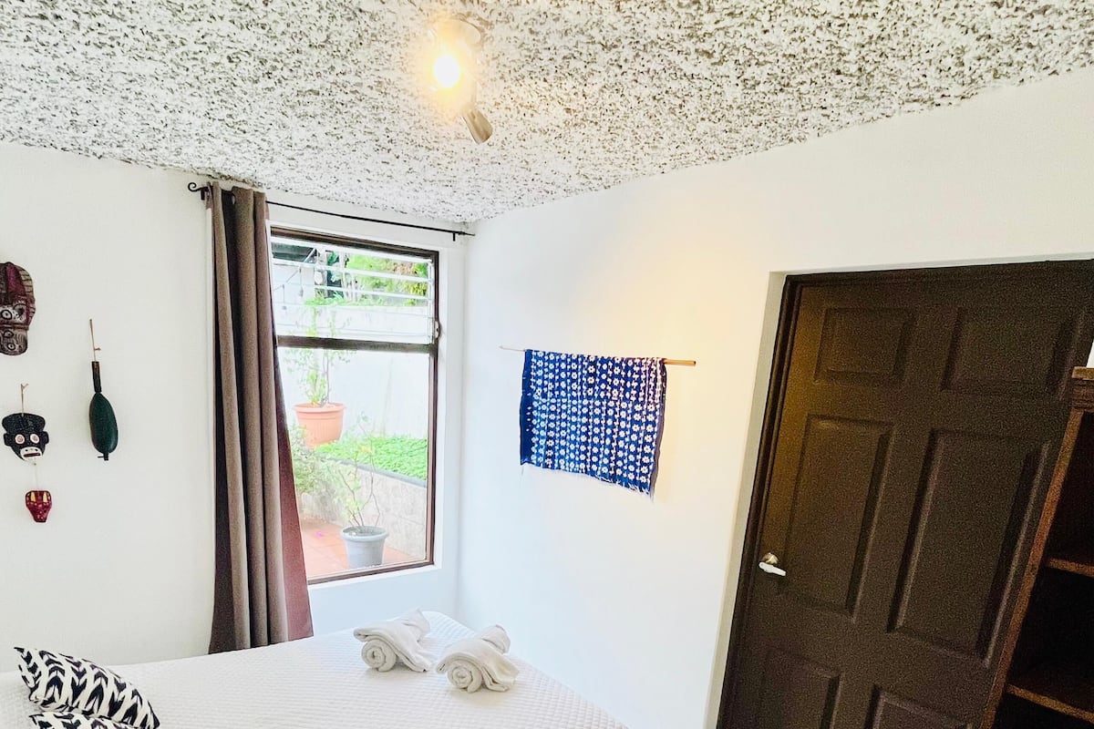 Un dormitorio con cama, ventana, puerta y techo con diseño texturizado.