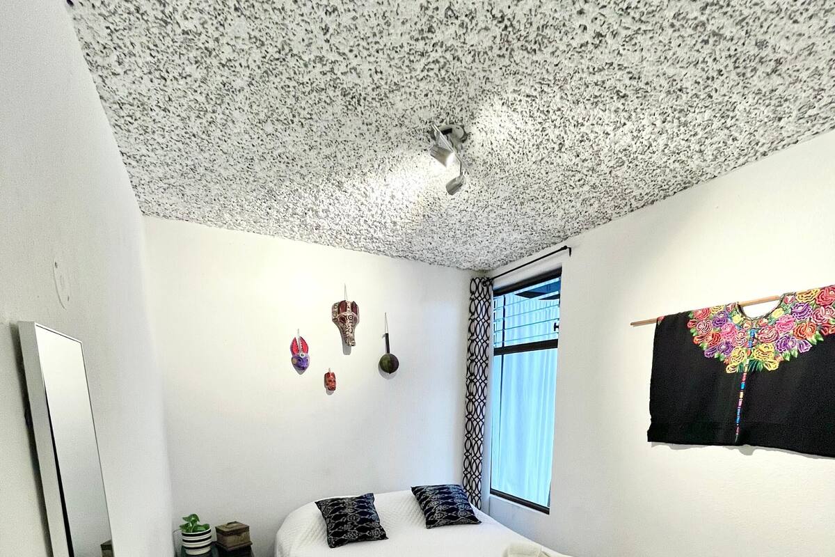 Un dormitorio con cama, ventana con vistas, techo con diseño moteado y pared decorada.